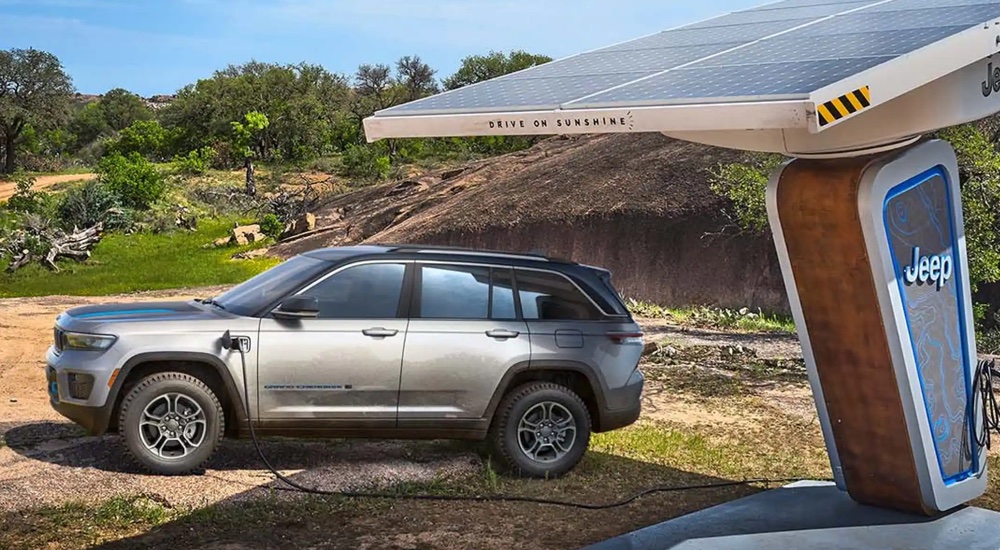 A silver 2022 Jeep Grand Cherokee 4xe is shown from the side parked at a charging station.