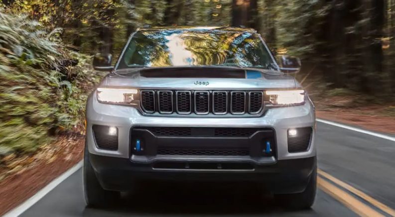 A silver 2022 Jeep Grande Cherokee 4xe is shown from the front driving on a tree-lined road.