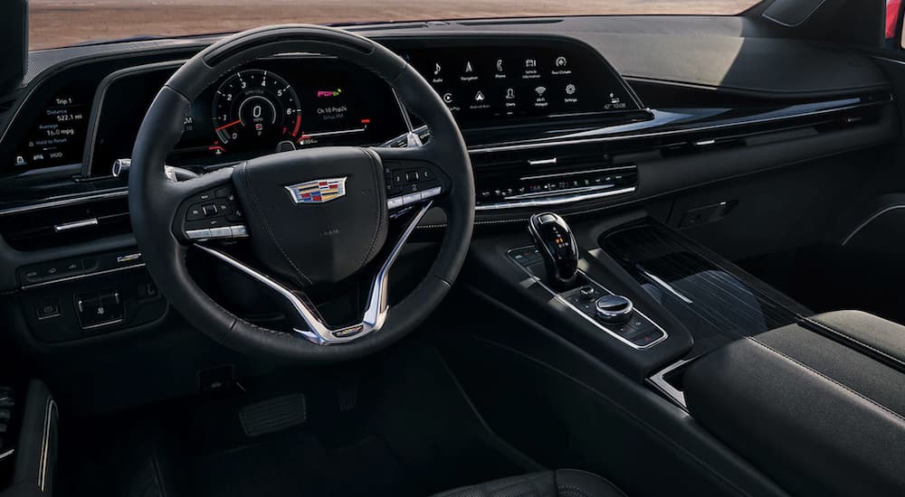 The black interior of a 2023 Cadillac Escalade V shows the steering wheel and infotainment screen.