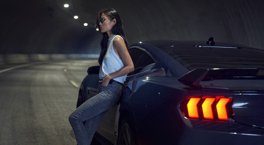 A person is shown leaning against a dark blue 2024 Ford Mustang Dark Horse parked in a tunnel.