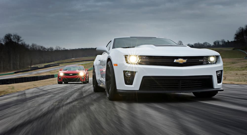 A white and a red 2014 Chevy Camaro ZL1 are shown on a race track.