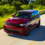 A popular Dodge Durango for sale, a maroon 2022 Dodge Durango SRT 392, is shown driving on a tree-lined road.