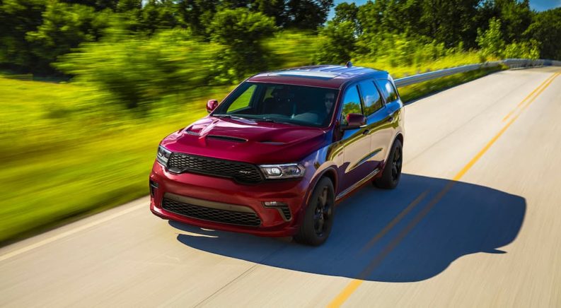 A popular Dodge Durango for sale, a maroon 2022 Dodge Durango SRT 392, is shown driving on a tree-lined road.