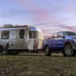 A blue 2023 Ford Ranger Lariat is shown parked in front of a silver camper.