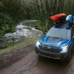 A blue 2023 Subaru Forester Wilderness is shown driving on a dirt road after leaving a Subaru Forester dealer.