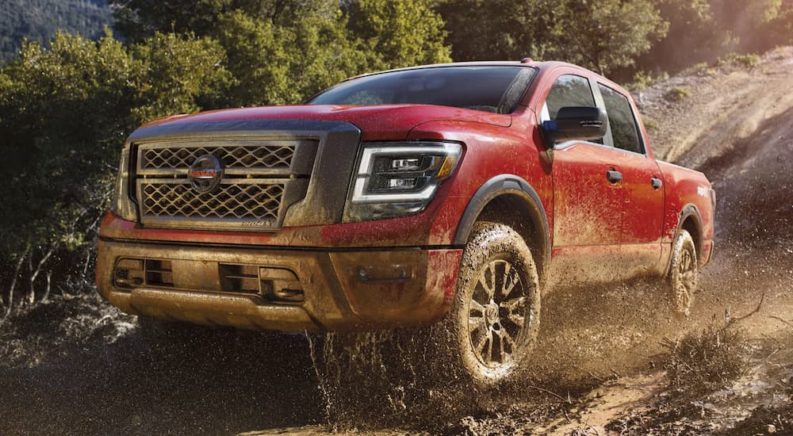 A red 2021 Nissan Titan XD Pro-4x is shown driving through a muddy puddle.