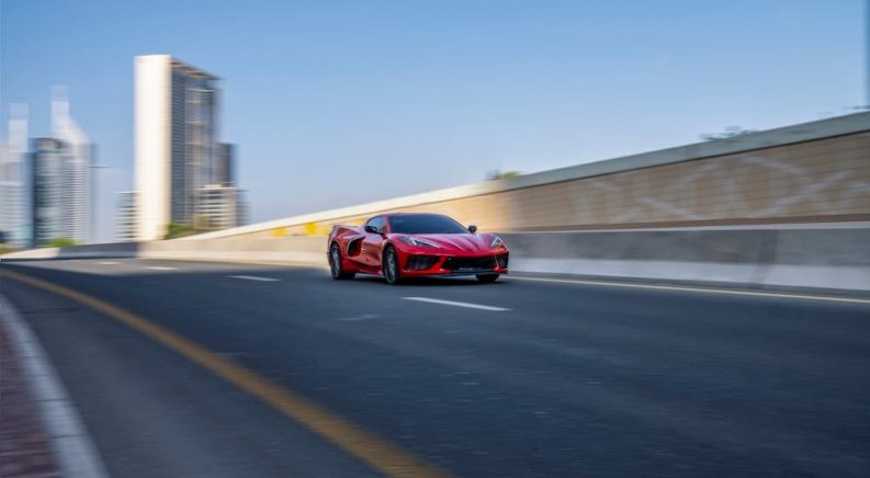 A red 2023 Chevy Corvette Stingray is shown driving on a city highway.