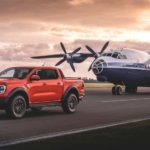 An orange 2023 Ford Ranger Raptor is shown on a runway next to a airplane.