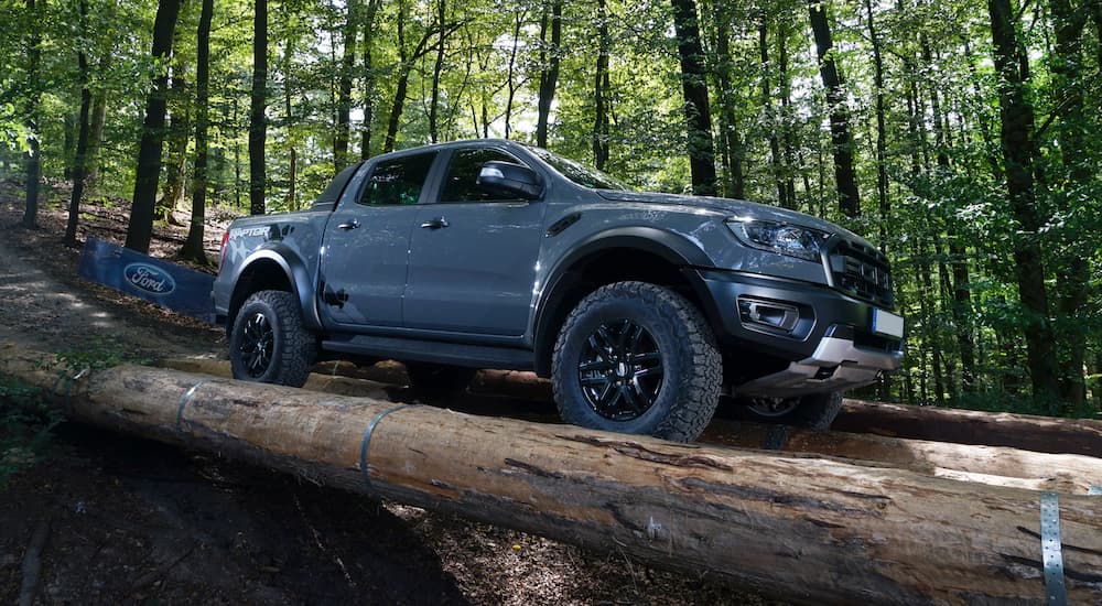 A grey 2023 Ford Ranger Raptor is shown driving over a log bridge in the woods.