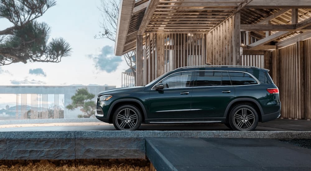 A green 2023 Mercedes GLS SUV is shown from the side parked near a wooden structure.