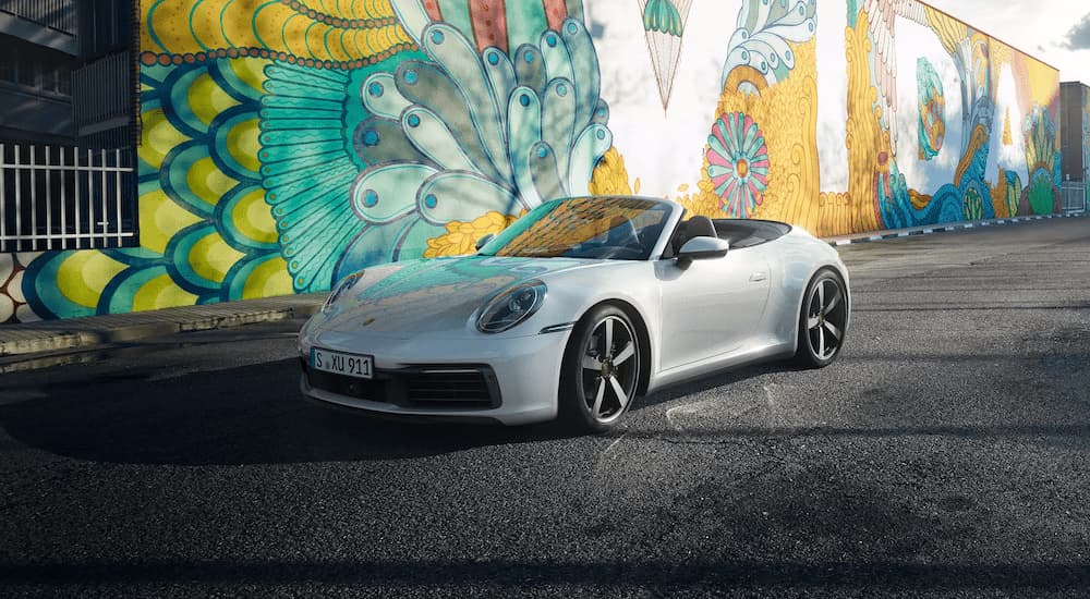 A silver 2023 Porsche 911 Carrera is shown parked next to a painted mural.