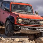 A red 2022 Ford Bronco Raptor is shown off-roading on a rocky trail.