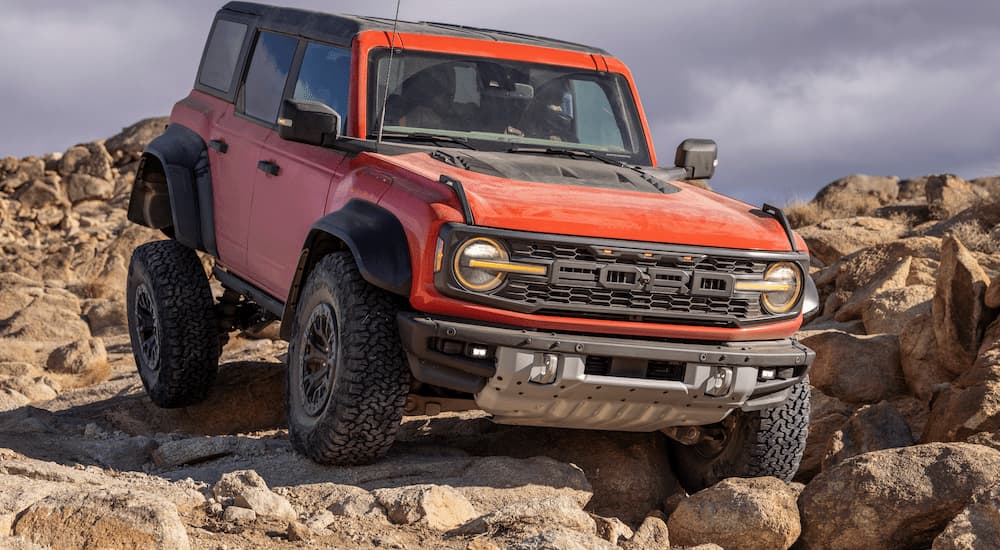 A red 2022 Ford Bronco Raptor is shown off-roading on a rocky trail.