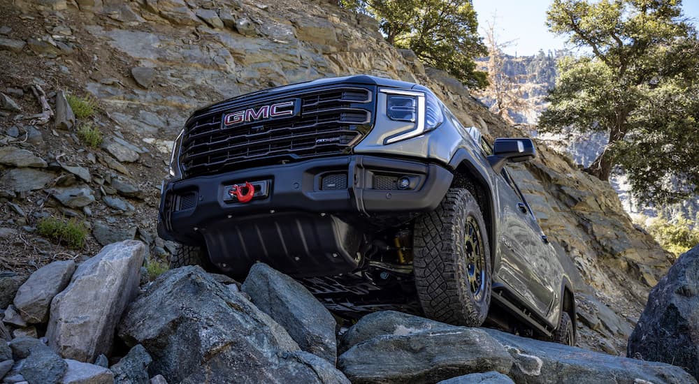 A grey 2023 GMC Sierra 1500 AT4X AEV Edition is shown from a low angle crawling over rocks.