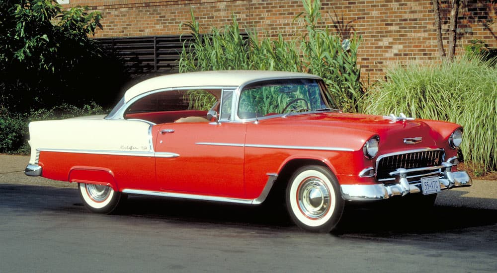 A red and white 1955 Chevy Bel-Air Sport Coupe is shown parked on pavement.