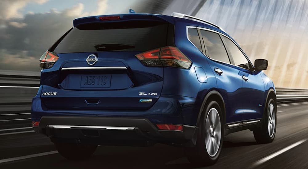 A blue 2017 Nissan Rogue for sale, is shown driving over a bridge.