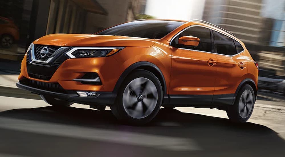 A popular used Nissan Rogue for sale, an orange 2021 Nissan Rogue, is shown rounding a corner.