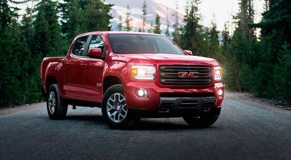 A red 2019 GMC Canyon is shown parked in the middle of a tree-lined road.