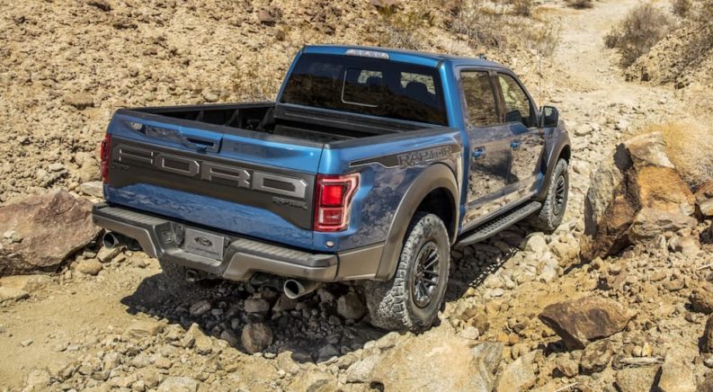 A blue 2020 Ford F-150 Raptor is shown from the rear while driving on a rocky trail.