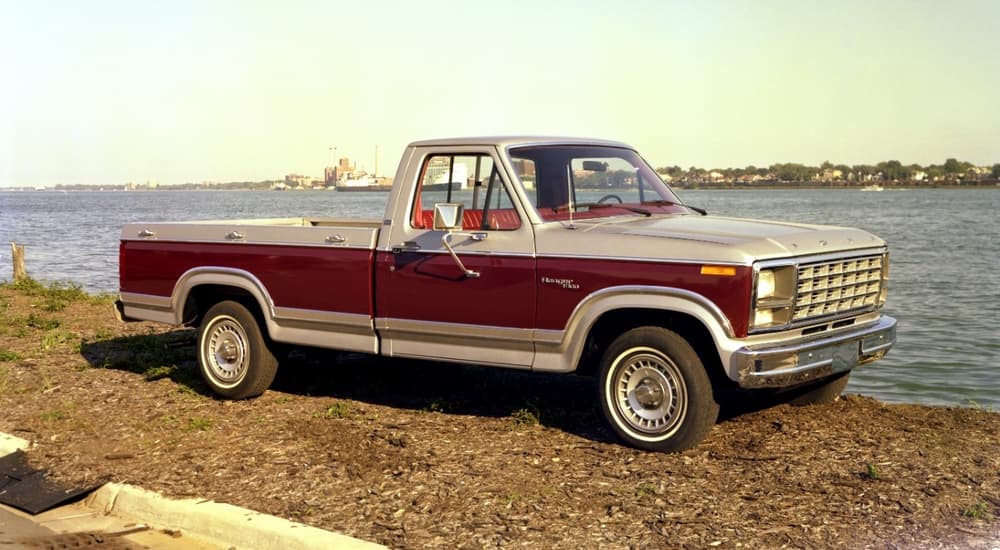 A red 1980 Ford F-100 is shown parked next to an ocean.