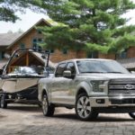 A white 2016 Ford F-150 Limited is shown towing a boat after leaving a used truck dealer.