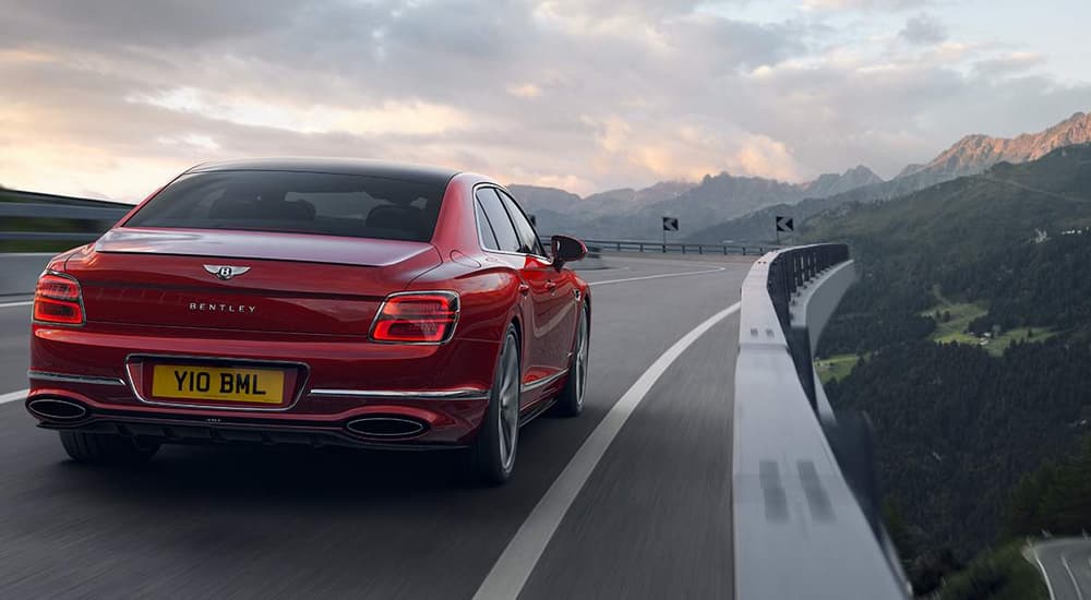 A red 2023 Bentley Flying Spur is shown from a rear angle driving on a highway overpass.