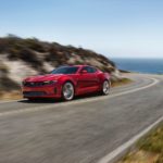 A red 2023 Chevy Camaro LT1 is shown driving on a coastal road.