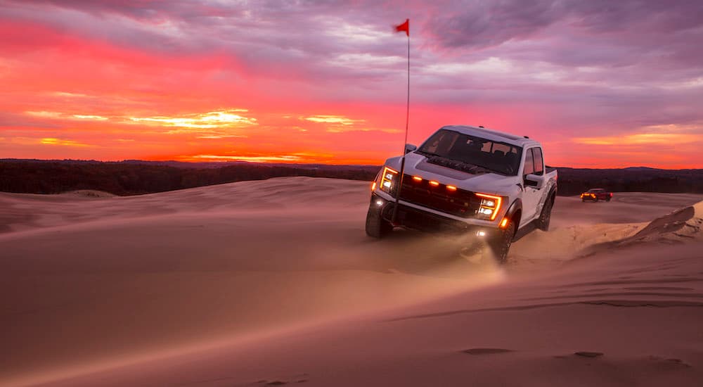 A white 2023 Ford F-150 Raptor R is shown from the front while driving through sand.
