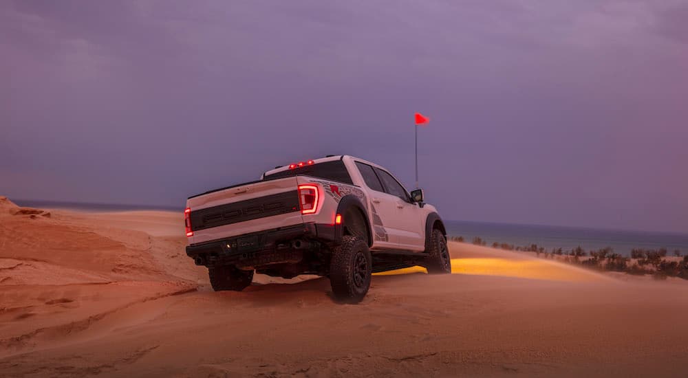 A white 2023 Ford F-150 Raptor R is shown from the rear while driving through sand.