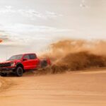 A red 2023 Ford F-150 Raptor R is shown from the side while driving through sand after leaving a Ford F-150 dealer.
