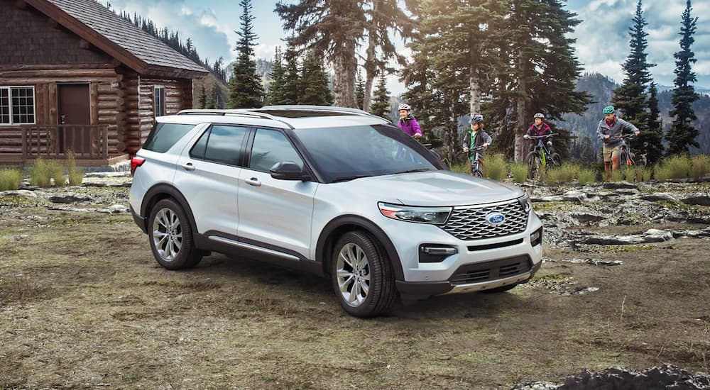 A white 2023 Ford Explorer is shown parked near a cabin and family on bikes.