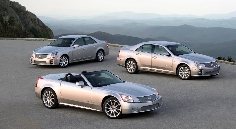 A silver 2006 Cadillac CTS-V, XLR-V, and STS-V are shown parked on a mountain lot.