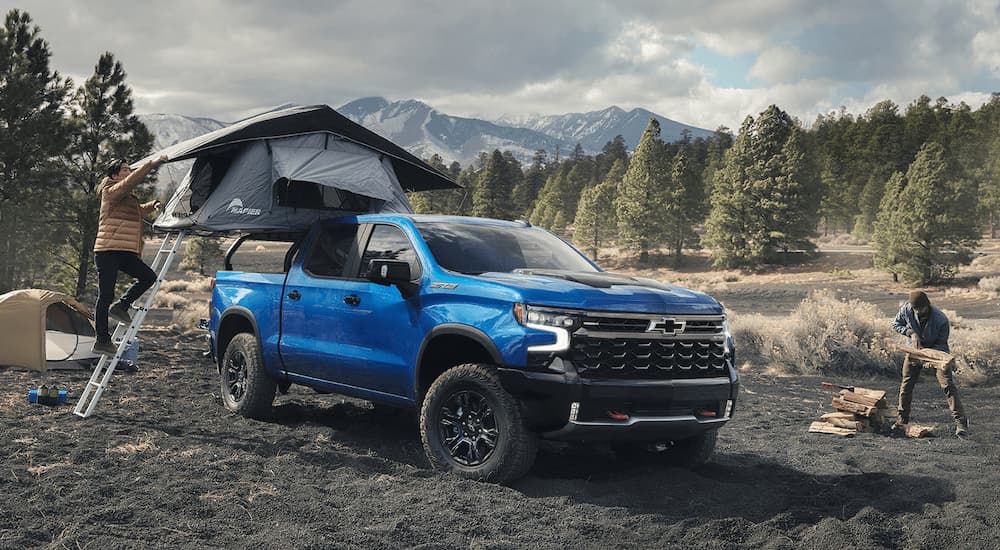A blue 2023 Chevy Silverado 1500 ZR2 is shown parked at a remote campsite with a mountain view.
