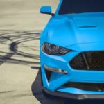 A close up shows the front end of a blue 2023 Ford Mustang next to tire marks.