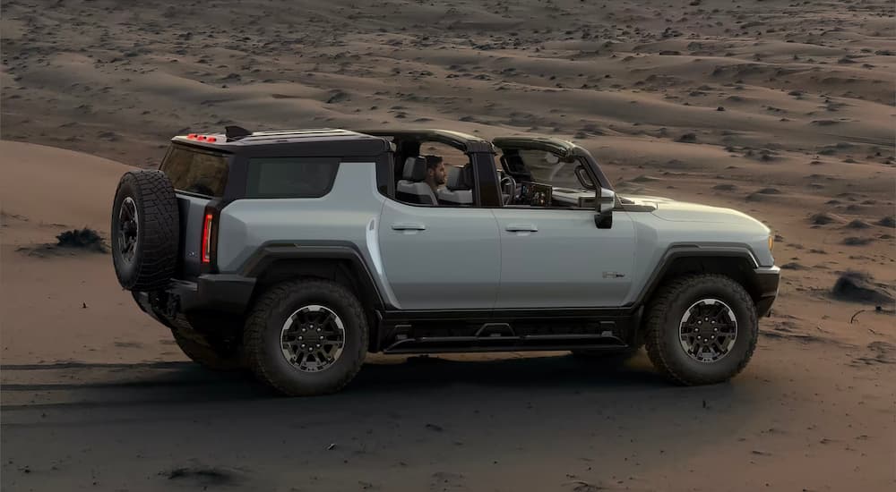 A white 2024 GMC Hummer EV is shown from the side driving over sand.