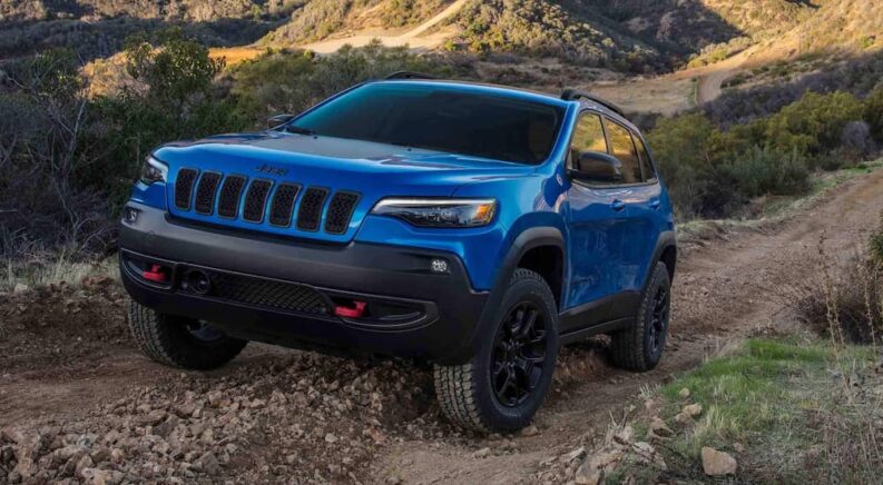 A blue 2022 Jeep Cherokee Trailhawk is shown driving up a rocky hill.