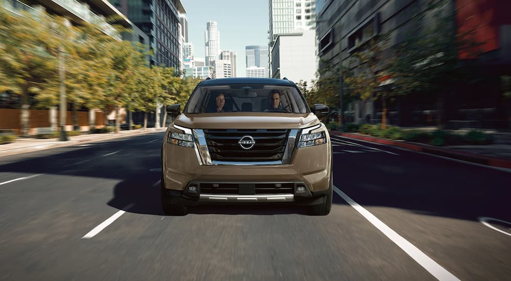 A brown 2023 Nissan Pathfinder is shown from the front driving on a city street.