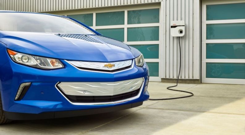 A blue 2016 Chevy Volt is shown charging at a use car lot.