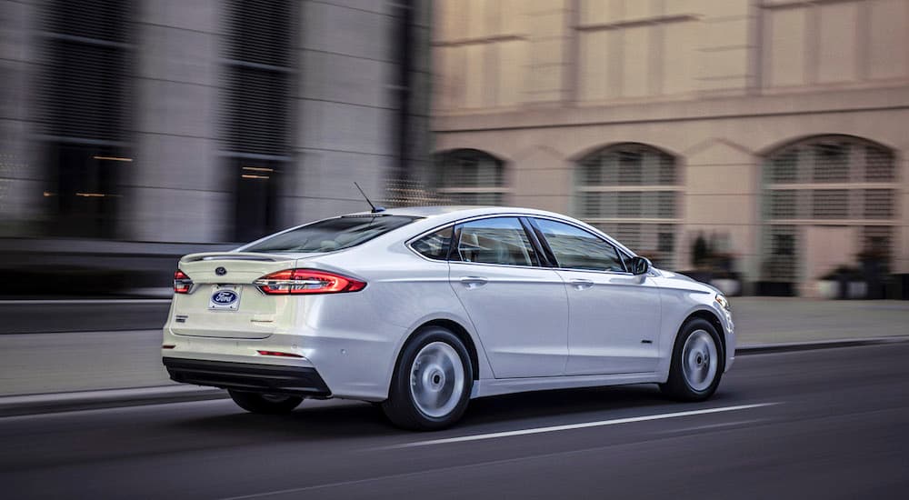 A white 2020 Ford Fusion Hybrid is shown from the side driving on a city street.