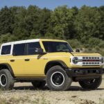 A yellow 2023 Ford Bronco Heritage Edition is shown parked on a dirt path.