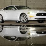 A white 2023 Ford Mustang GT is shown parked near a puddle.