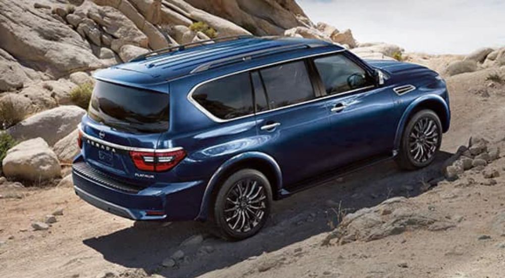 A blue 2023 Nissan Armada is shown driving up a rocky off-road trail. 