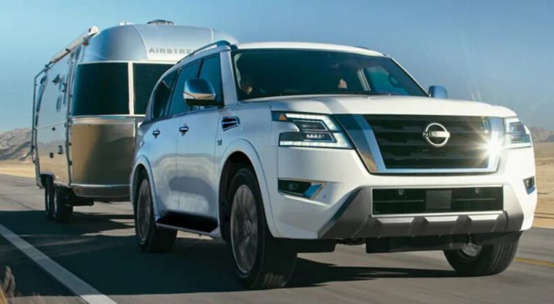 A white 2023 Nissan Armada for sale is shown towing a camper down an open road.