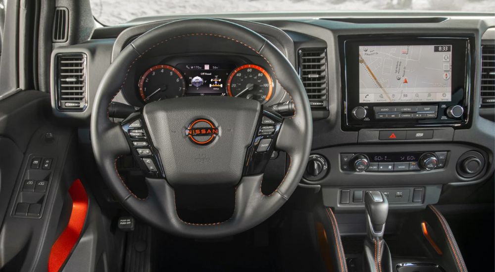 Shows the wheel, driver information display, and infotainment screen of the 2023 Nissan Frontier.