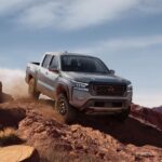 A grey 2023 Nissan Frontier for sale is shown off-roading down a dirt trail.