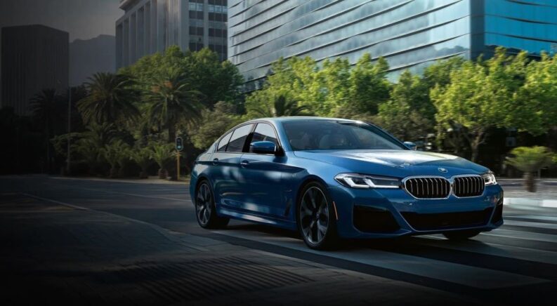 A blue 2023 BMW 530e is shown driving on a city street.