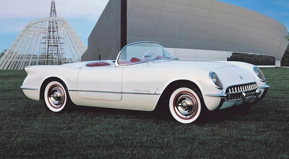 A white 1953 Chevrolet Corvette is shown parked on the grass near a Chevy dealer.