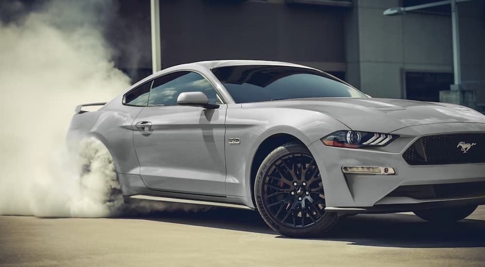 A white 2023 Ford Mustang GT does a burnout in a parking lot.