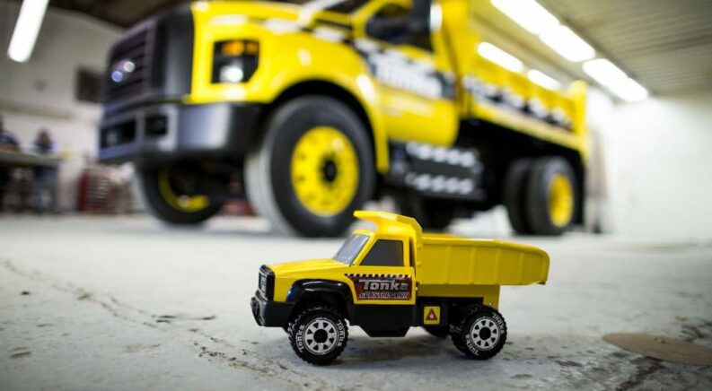 A close up of a yellow Tonka truck is shown in front of a yellow 2014 Ford F-750 Tonka Edition for sale.