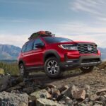 A red 2023 Honda Passport TrailSport is shown driving up a gravel mountain trail.